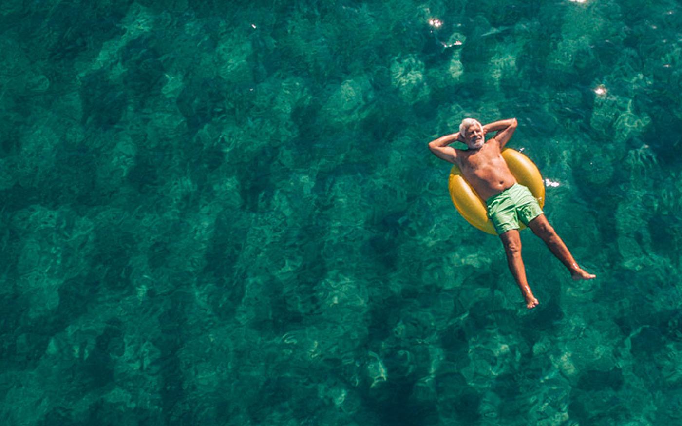 An older man relaxing and laying down in an inner tube on relaxing water.